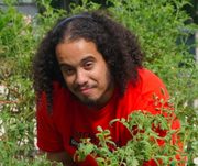 Returning AmeriCorps member Jesse Baez smiling outdoors in the community garden.