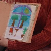 Hands holding an art journal page painted with trees, a house, and a window design.