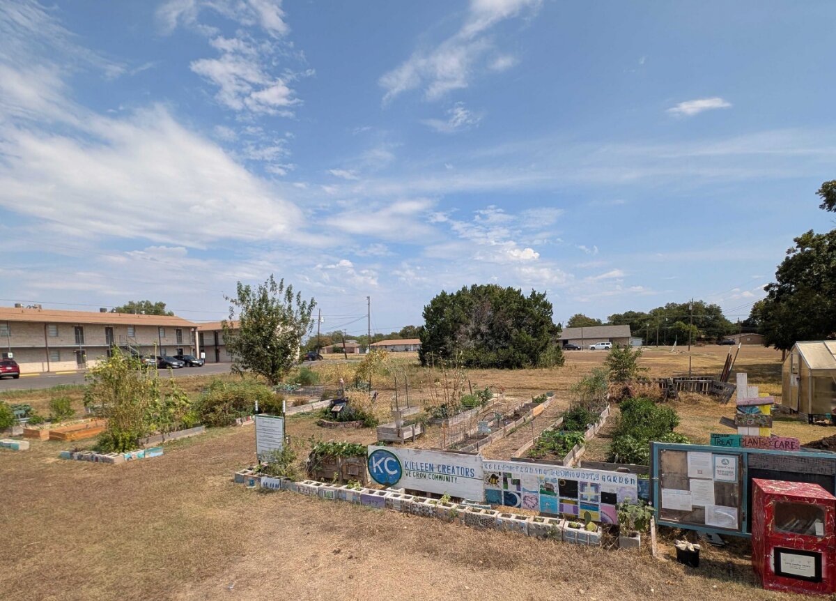 Raised garden beds and the Killeen Creators sign at the 10th Street Garden with the greenhouse behind.