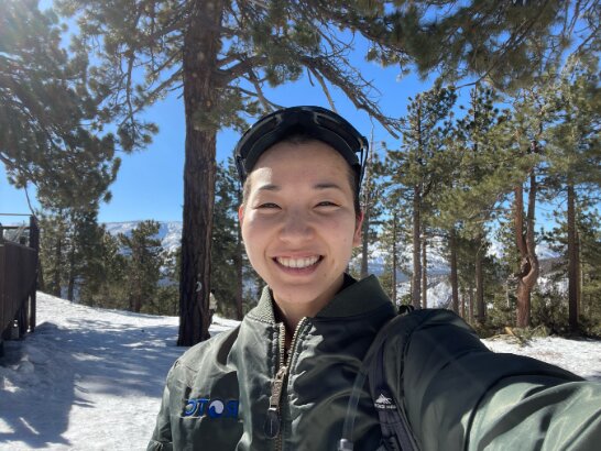 New AmeriCorps member Vivian Moon smiling on a snowy pine forest hike, ready to lead creative classes.